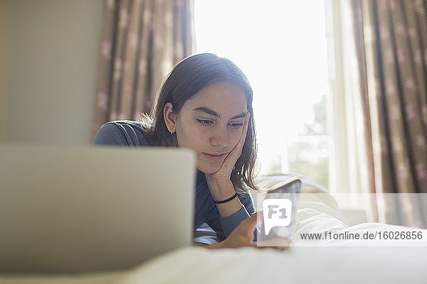 Teenagerin benutzt Smartphone am Laptop im Bett