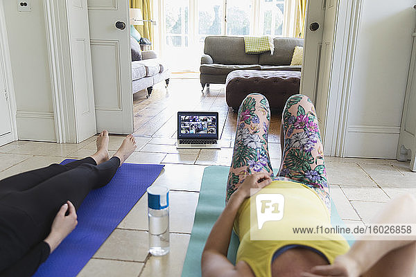 Frauen praktizieren Yoga online mit dem Laptop zu Hause
