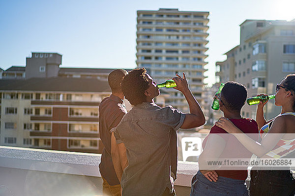 Junge Freunde trinken Bier auf dem sonnigen Stadtdach