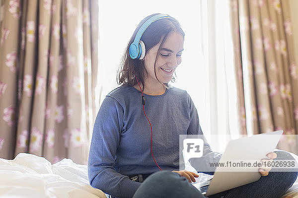 Teenagerin mit Kopfhörern und Laptop Video-Chat im Bett