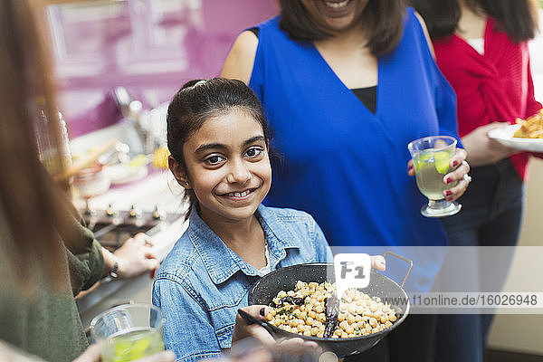 Porträt eines lächelnden indischen Mädchens  das mit seiner Familie in der Küche das Essen zubereitet