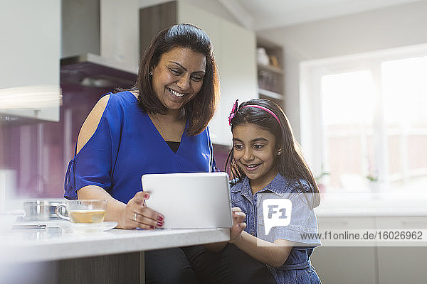 Glückliche Mutter und Tochter benutzen digitales Tablett in der Küche