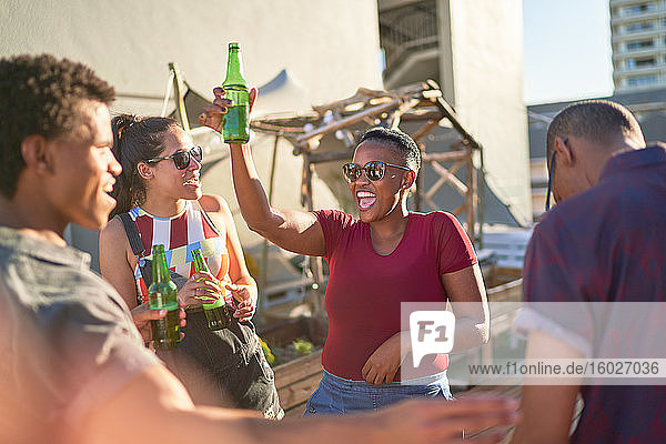 Fröhliche junge Freunde tanzen und trinken Bier auf dem sonnigen Balkon