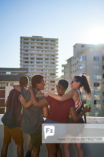 Glückliche junge Freunde hängen auf dem sonnigen Balkon auf dem städtischen Dach herum