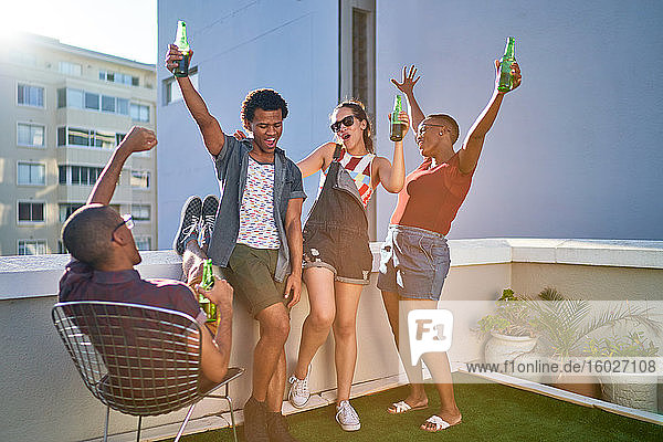 Fröhliche junge Freunde jubeln und trinken Bier auf dem Dach der Stadt