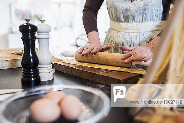 Frau wälzt Teig mit Nudelholz in der Küche