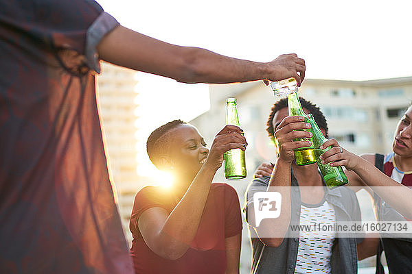 Junge Freunde stoßen auf Biergläser auf dem sonnigen Dach der Stadt an