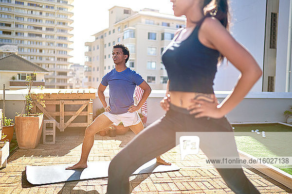 Young couple practicing yoga on sunny urban rooftop