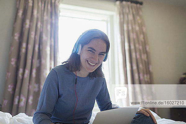 Porträt eines glücklichen Teenager-Mädchens mit Kopfhörern und digitalem Tablet auf dem Bett