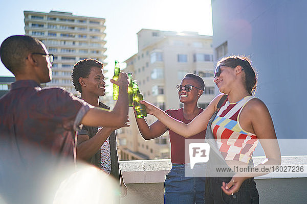 Happy young friends drinking beer on sunny urban rooftop