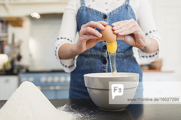 Teenager-Mädchen bricht Ei in der Küche in eine Schüssel zum Backen
