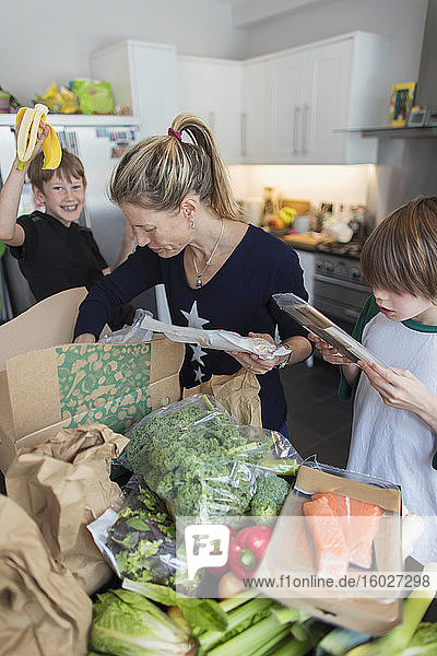 Frau und Söhne entladen frische Produkte aus der Kiste in der Küche
