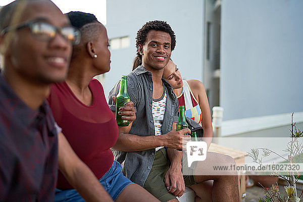 Porträt eines selbstbewussten jungen Mannes  der mit Freunden auf der Terrasse Bier trinkt