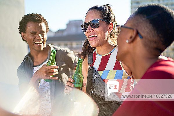 Glückliche junge Freunde trinken Bier auf dem sonnigen Balkon