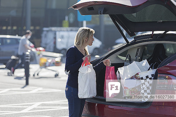 Frau lädt Lebensmittel auf sonnigen Parkplatz in den Kofferraum ihres Autos