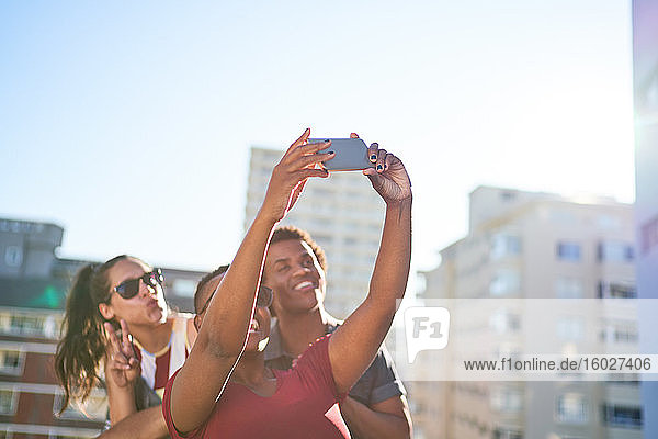 Junge Freunde beim Selbstfahren mit dem Smartphone auf dem sonnigen Stadtdach