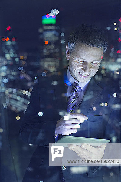 Geschäftsmann benutzt digitales Tablet im Stadtfenster bei Nacht