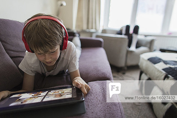 Junge mit Kopfhörern und digitalem Tablet Heimunterricht auf dem Sofa
