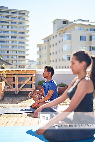Junger Mann und Frau praktizieren Yoga auf einem sonnigen städtischen Dach