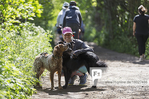 Glückliche Frau wandert mit Hunden auf sonnigem Pfad