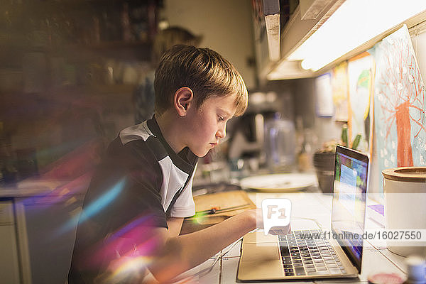 Focused boy doing homework at laptop in kitchen
