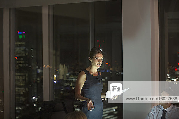 Businesswoman leading meeting in conference room at night