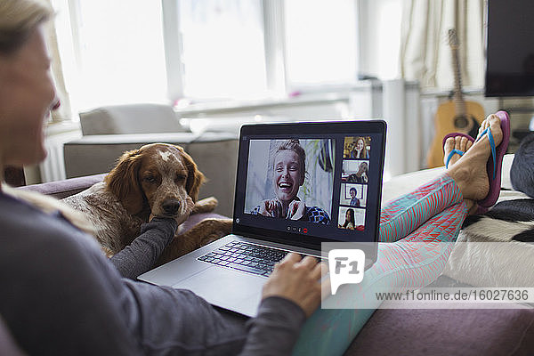 Woman with laptop video chatting with friends on sofa with dog
