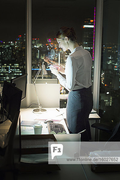 Businesswoman text messaging with cell phone in office at night