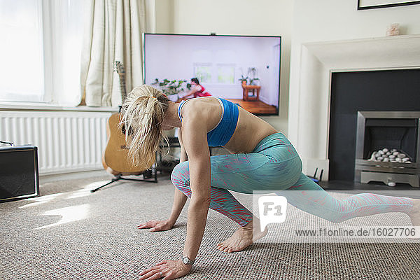 Frau praktiziert Online-Yoga im Wohnzimmer