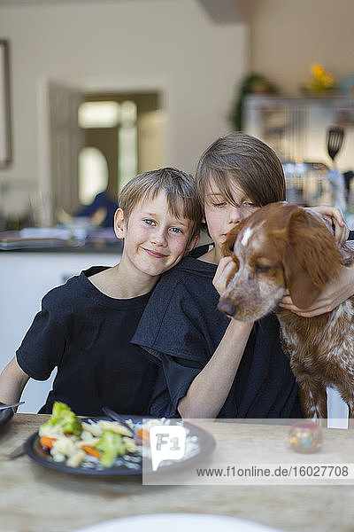 Portrait brothers with dog eating at dining table