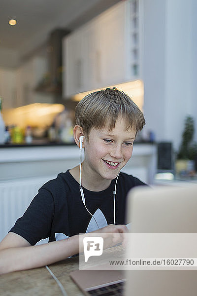 Lächelnder Junge mit Kopfhörern beim Heimunterricht am Laptop