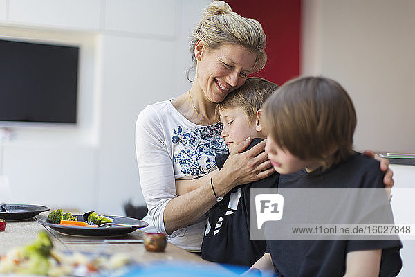 Affectionate mother hugging sons at dinner table