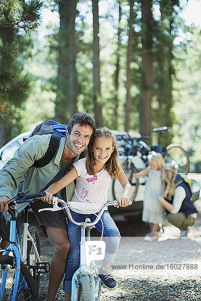 Smiling father and daughter on bicycles in woods