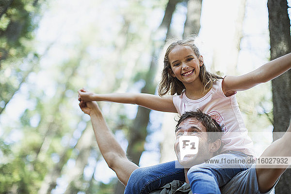 Father carrying daughter on shoulders in woods