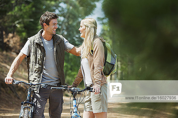Lächelndes Paar mit Mountainbikes im Wald
