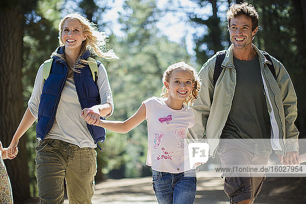 Lächelnde Familie hält Händchen und rennt im Wald