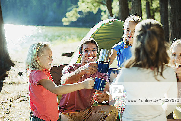 Lächelnde Familie röstet Tassen auf dem Campingplatz