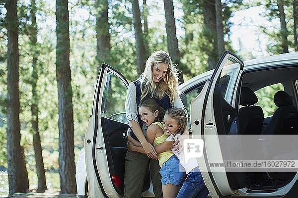 Mutter umarmt Töchter vor dem Auto im Wald