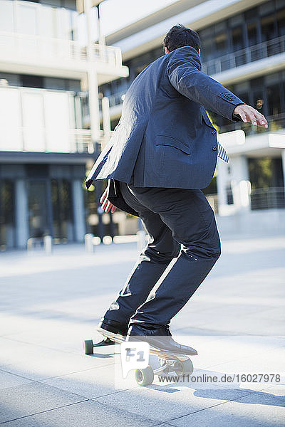 Geschäftsmann beim Skateboarden auf dem städtischen Bürgersteig