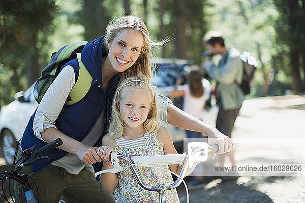 Smiling mother and daughter with bicycle in woods