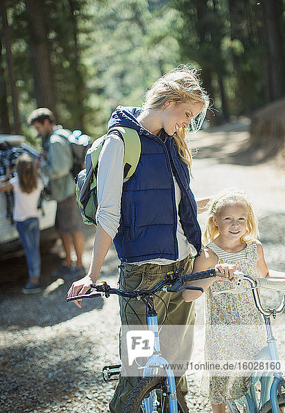 Lächelnde Mutter und Tochter mit Fahrrädern im Wald