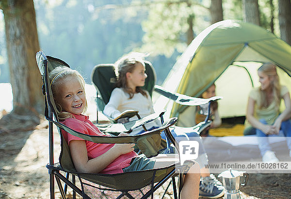 Lächelndes Mädchen sitzt auf einem Stuhl auf einem Campingplatz