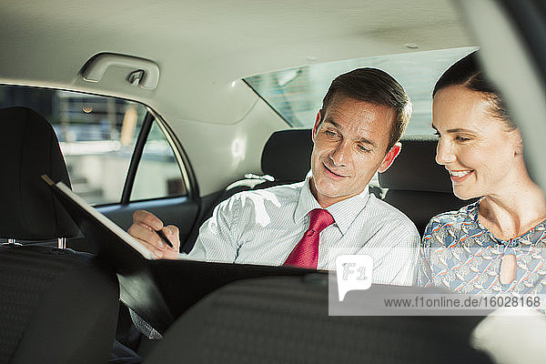Businessman and businesswoman working in back seat of car