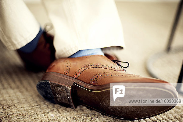 Close up of person's feet  wearing brown leather brogues  blue socks and white trousers.