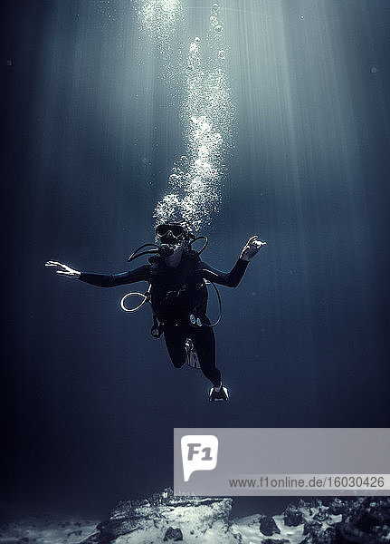 Underwater view of diver wearing wetsuit  diving goggles and oxygen cylinder  air bubbles rising.