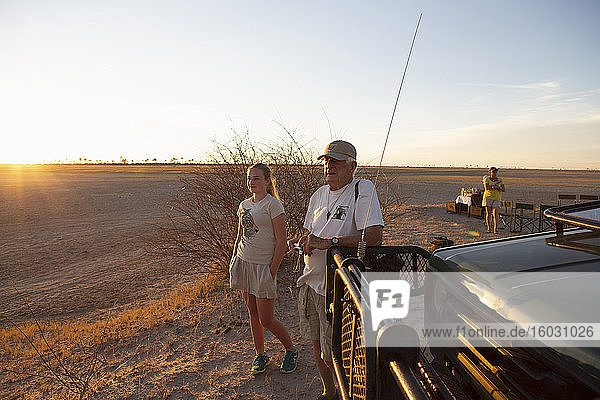 Ein Großvater und seine Enkelin schauen auf den Sonnenuntergang in der Kalahari-Wüste