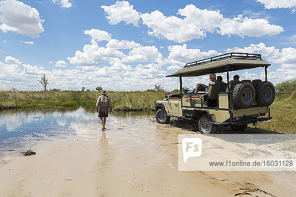 A safari vehicle with passengers  and a guide walking across sand
