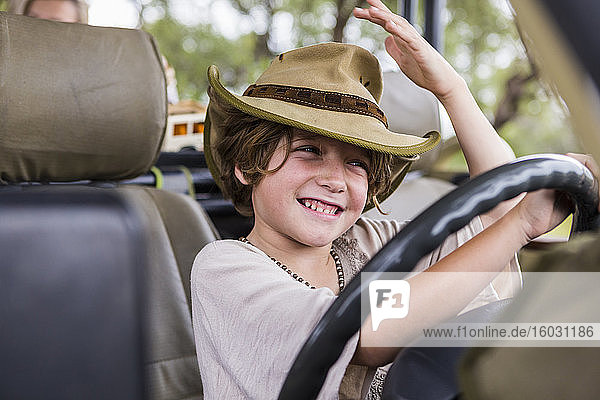 Lächelnder sechsjähriger Junge auf dem Fahrersitz eines Safari-Fahrzeugs.