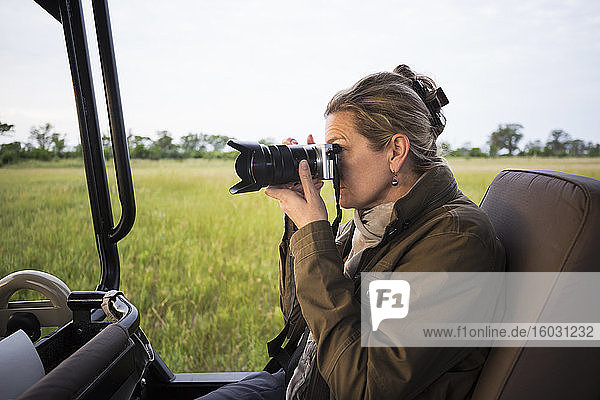Adult woman using camera seated in a safari jeep in open landscape