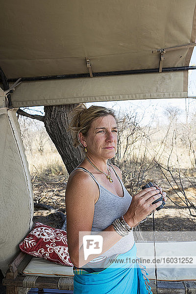 Eine erwachsene Frau mit einem Fernglas an einem Zelt in einem Wildreservat-Camp